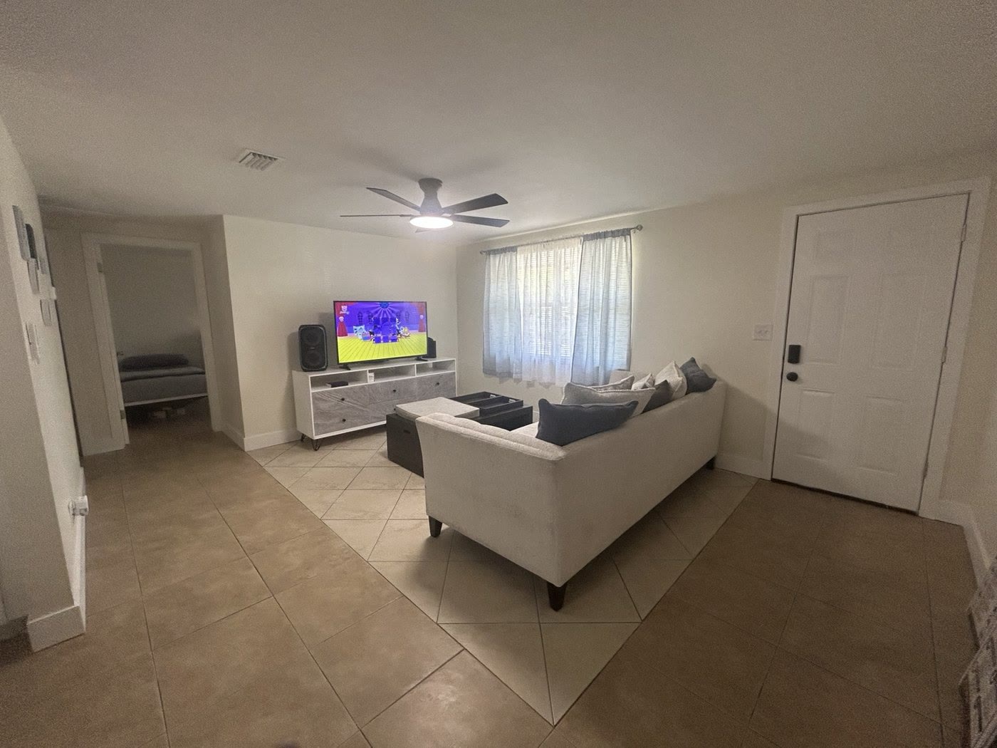 A living room with a white sofa, a TV on a stand and tile floors.